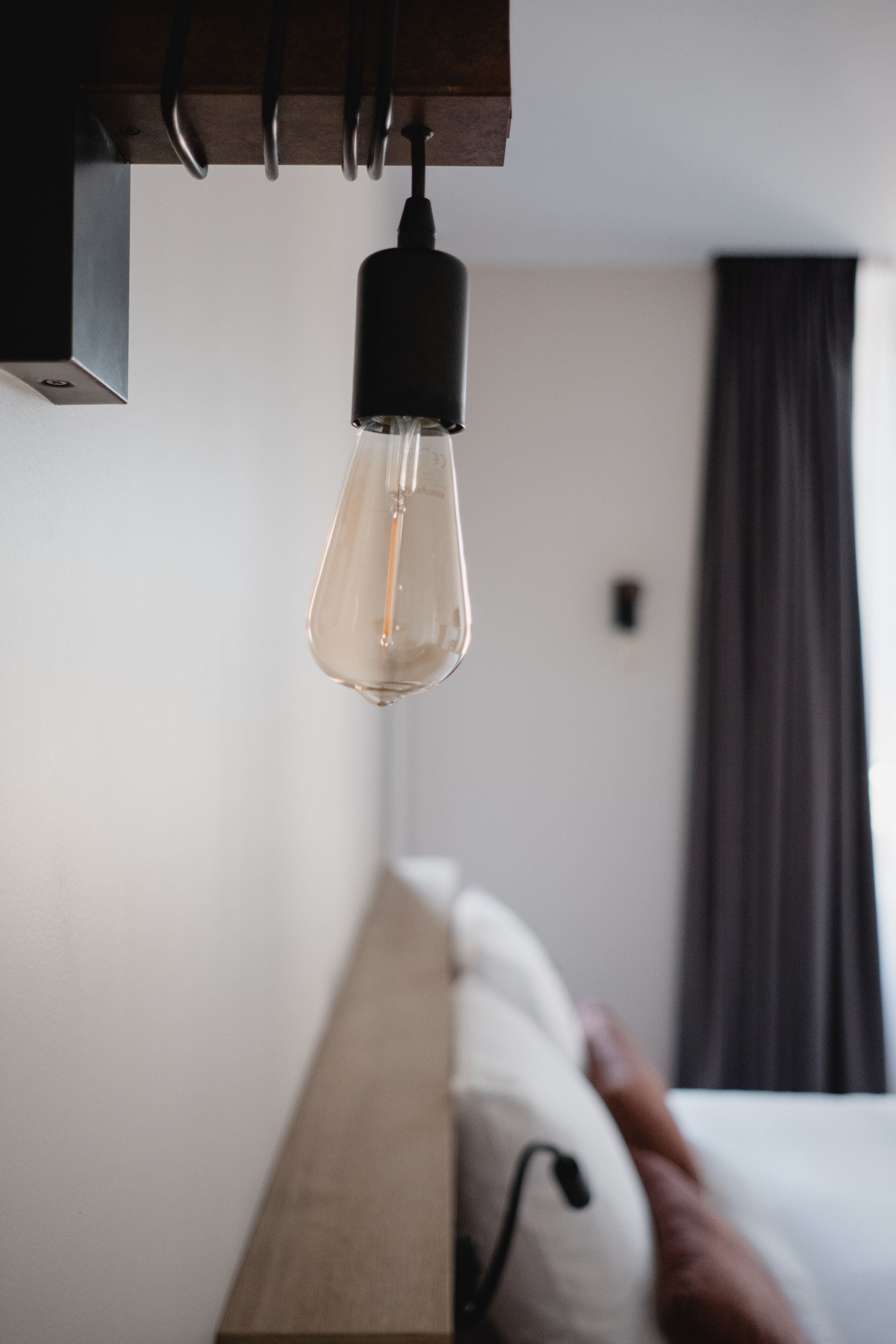 Une chambre d’hôtel moderne avec une tête de lit en bois, une ampoule suspendue et une fenêtre avec des rideaux.