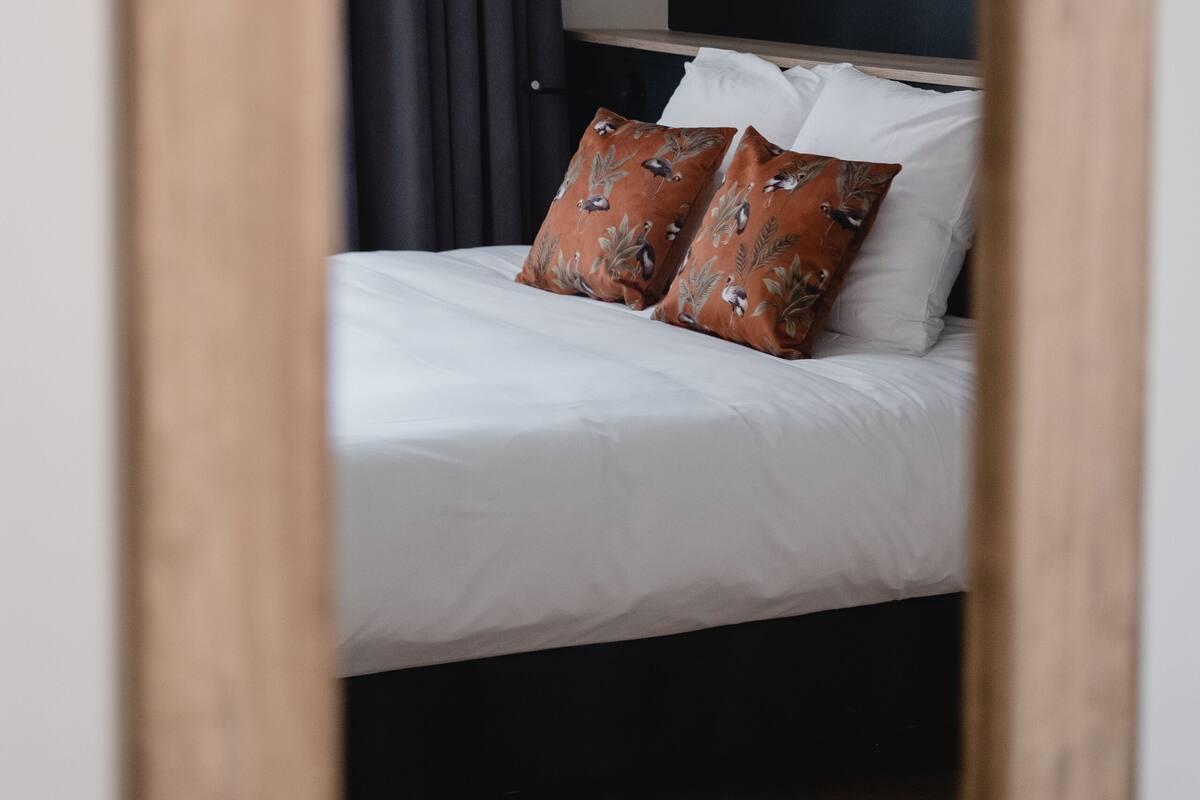 A bed with white bedding and two decorative pillows, a dark-colored headboard, and a ceiling fan.