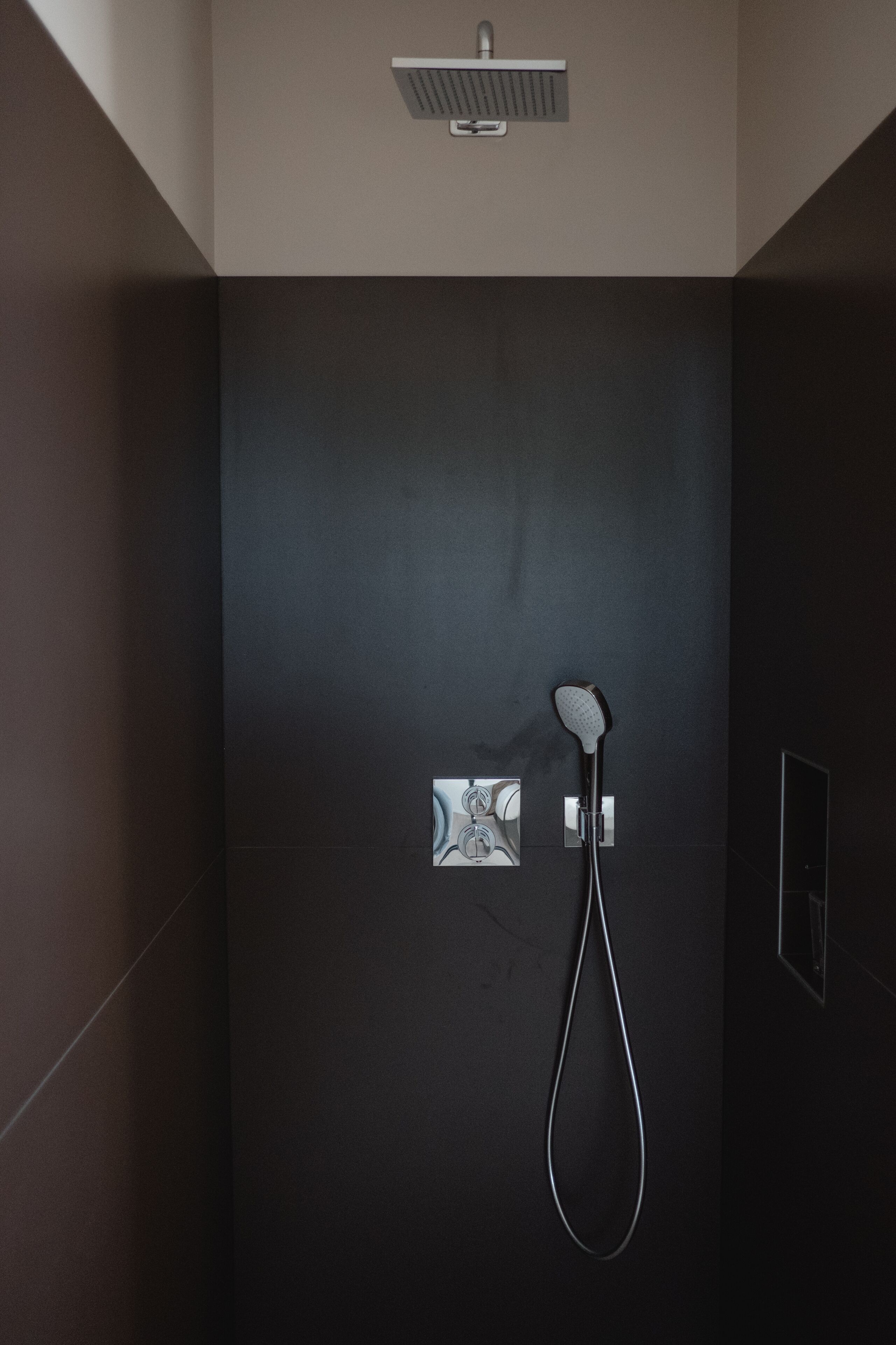 A modern shower area with a handheld showerhead and a wall-mounted control panel.