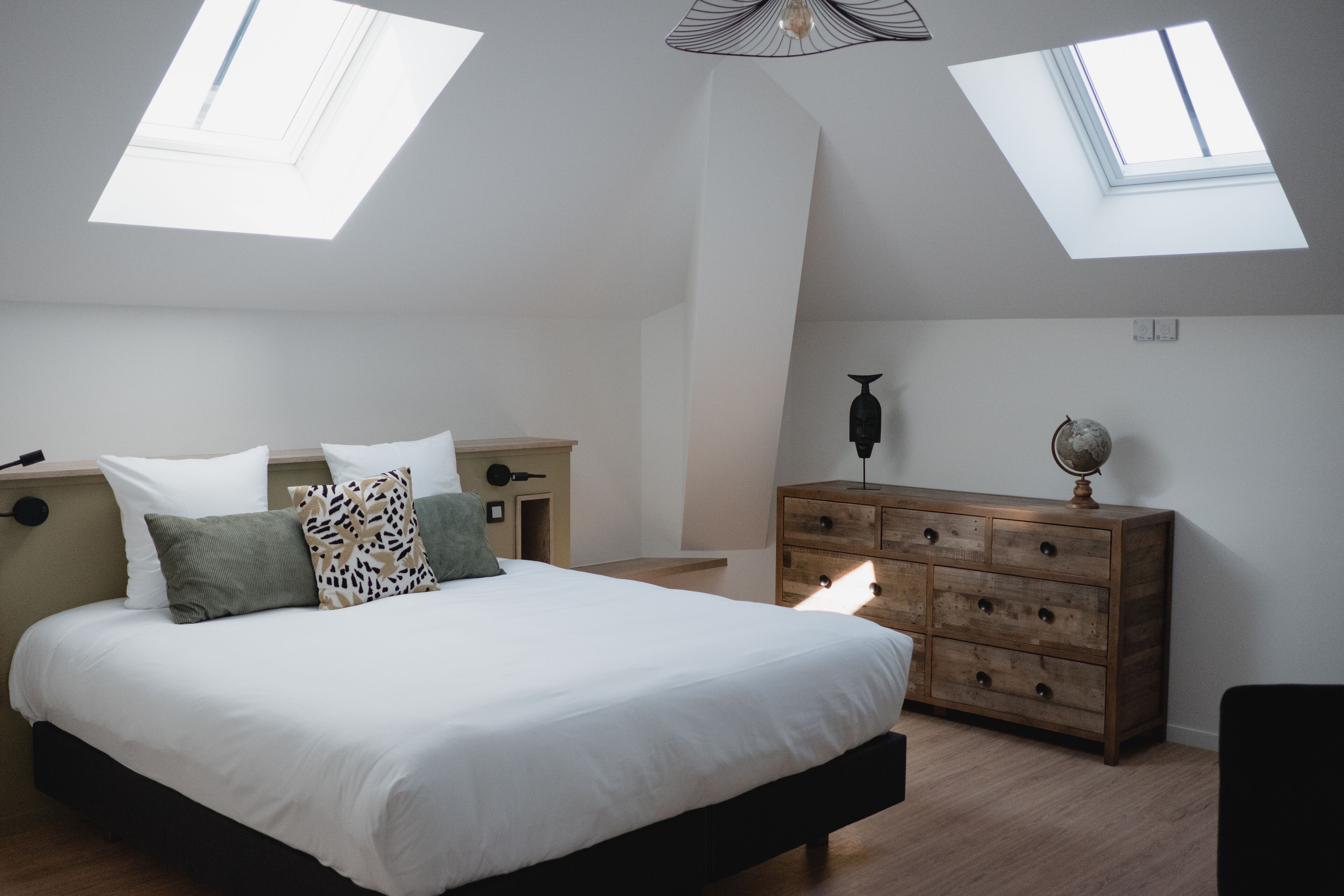 A bedroom with a large bed, a dresser, and a nightstand. There are skylights on the ceiling.