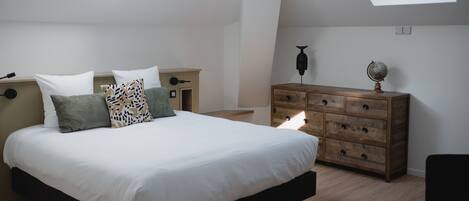 A bedroom with a large bed, a dresser, and a nightstand. There are skylights on the ceiling.