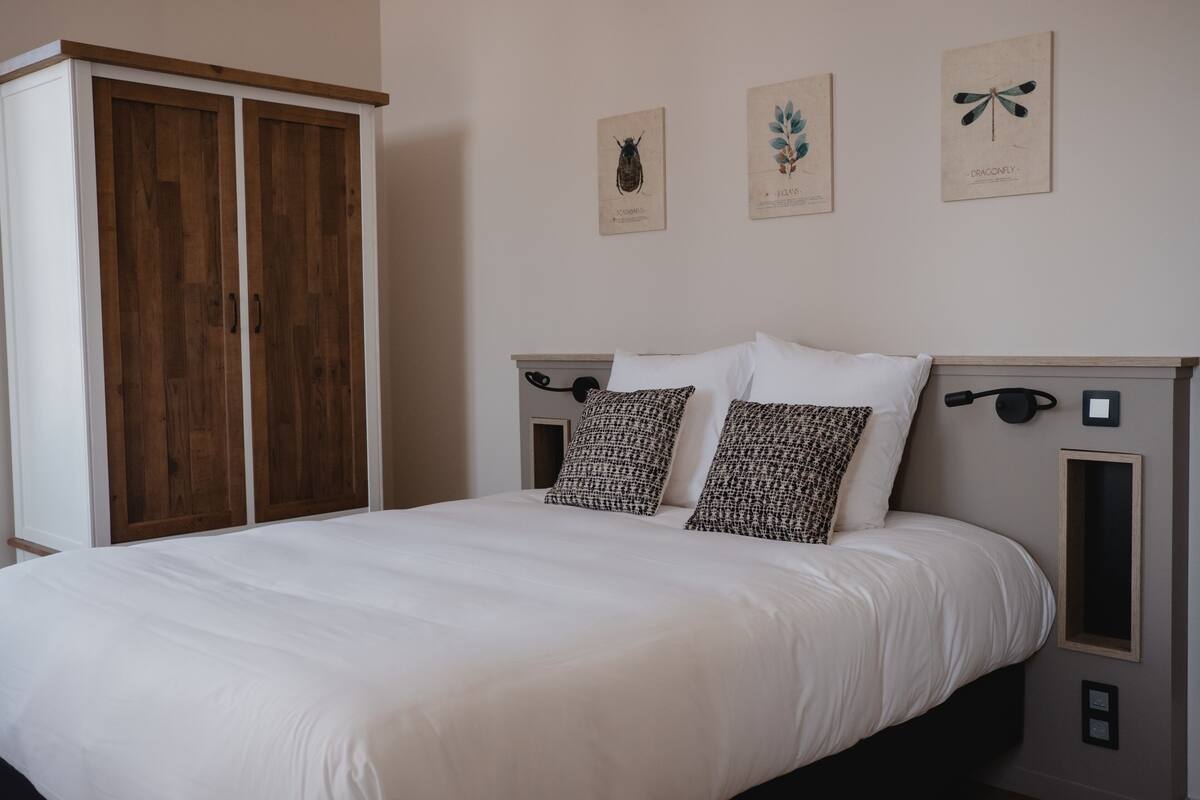 A bedroom with a bed, two pillows, a wardrobe, and three wall-mounted pictures.