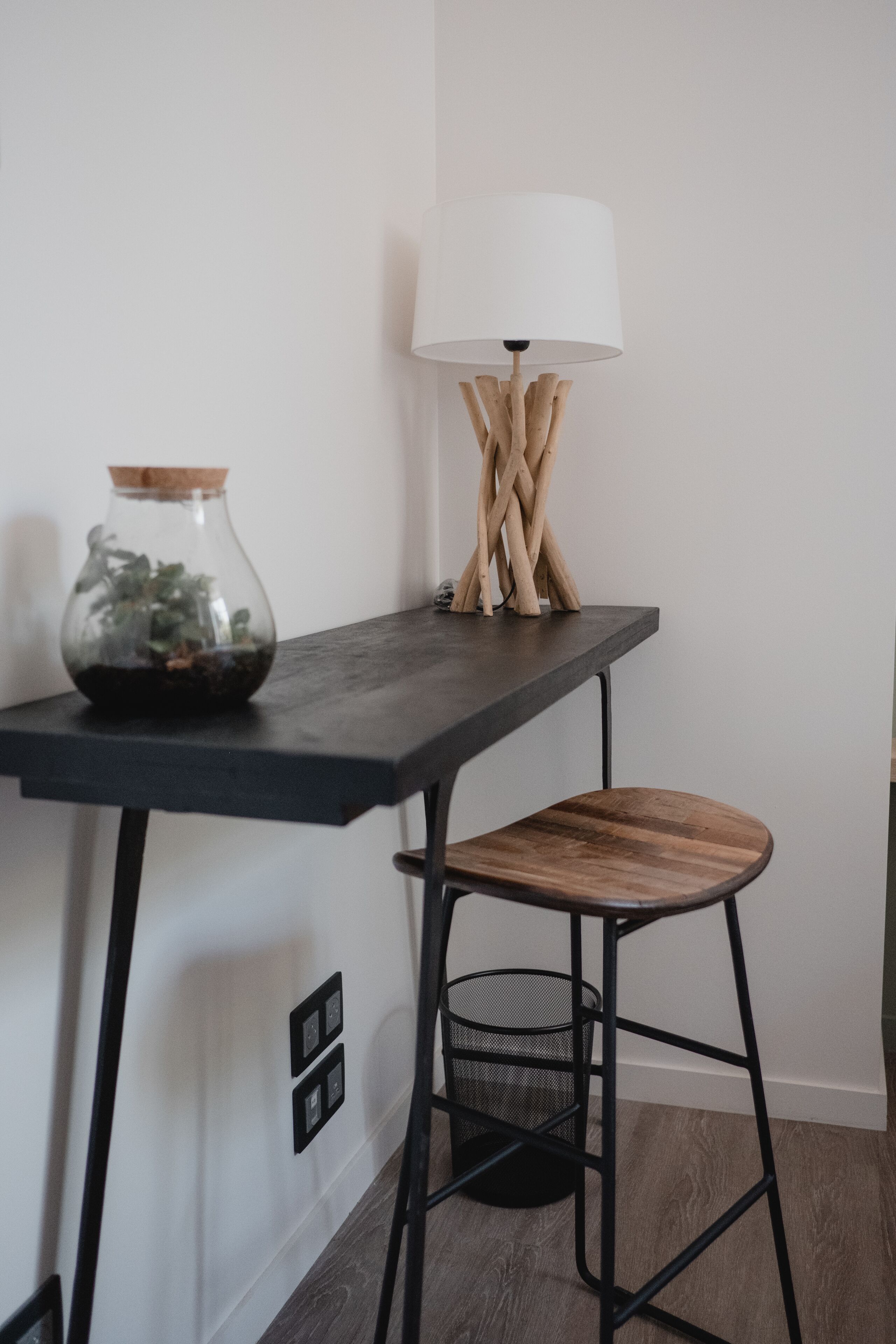 Eine moderne Küche mit dunkler Arbeitsplatte, einem Holzschemel, einer Glasvase mit Pflanzen und einer besonderen Lampe.