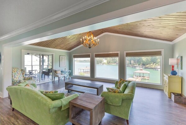 A spacious living room with a high ceiling and large windows overlooking a lake.