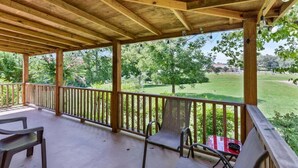 A covered patio with wooden beams, a wooden railing, and a view of a green landscape with trees and a golf course.