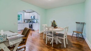 A dining area with a table and chairs, a kitchen in the background, and a ceiling light.