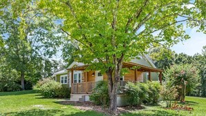A single-story house with a porch, surrounded by a well-maintained lawn and various shrubs.