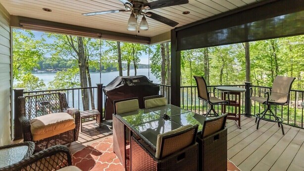 A covered outdoor area with a table and chairs, a ceiling fan, and a view of a lake.
