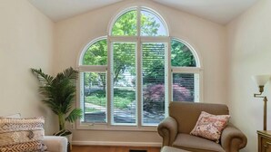 A cozy living room with a large arched window, a comfortable sofa, a chair, and a potted plant.