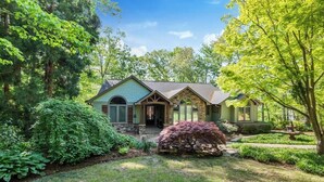 A house with a stone facade, a front porch, and a well-maintained garden with various shrubs and a large tree.
