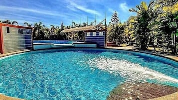 Una piscina con superficie de agua azul cristalina, rodeada de palmeras y un cielo despejado.