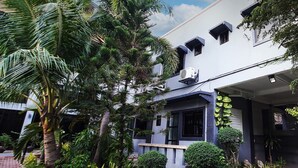 Un edificio moderno con techo plano, rodeado de abundante vegetación, incluyendo palmeras y arbustos diversos.