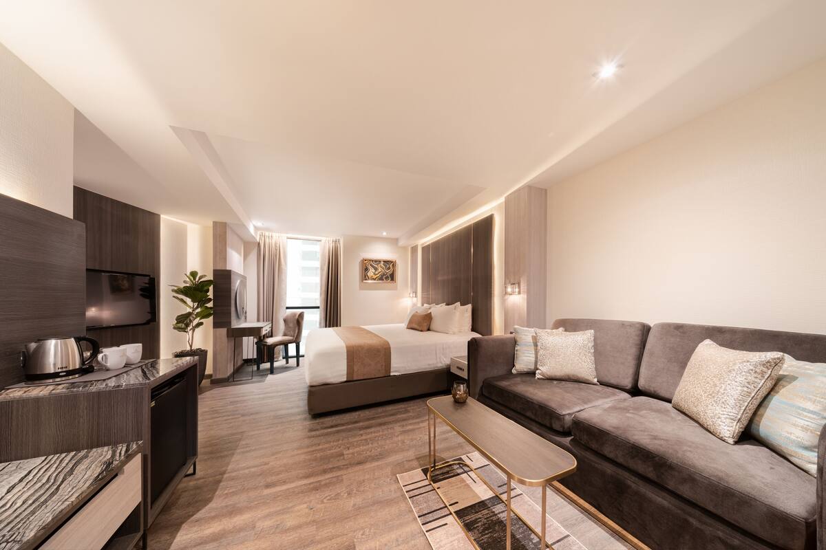 A modern hotel room with a bed, sofa, coffee table, and a small dining area.