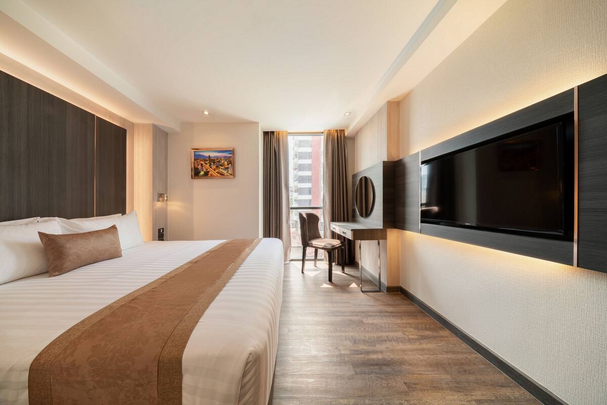 A modern hotel room with a large bed, a desk, a flat-screen TV, and a cityscape view.