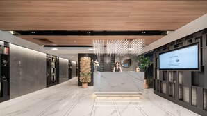 A modern hotel lobby with a marble reception desk, a large screen displaying the brand name, and a decorative wall with a plant. - Aspira Parc Sukhumvit 22 (Bangkok)
