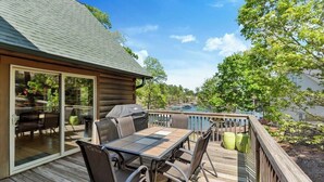 Une terrasse en bois avec une table et des chaises, un barbecue et une porte vitrée donnant sur un espace extérieur aménagé.
