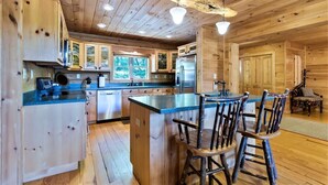 L’intérieur d’un chalet en bois comprend une cuisine avec un îlot central, des tabourets de bar et un coin repas avec une table et des chaises.