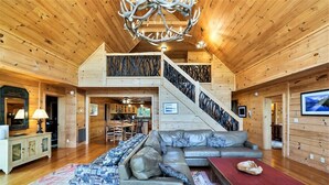 Un intérieur spacieux en bois, avec un grand canapé, un coin repas et un escalier menant à un niveau supérieur.