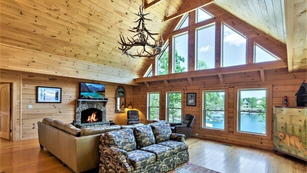 L’intérieur d’un chalet accueillant, avec une cheminée, un canapé, un divan à motifs et de grandes fenêtres donnant sur un lac.