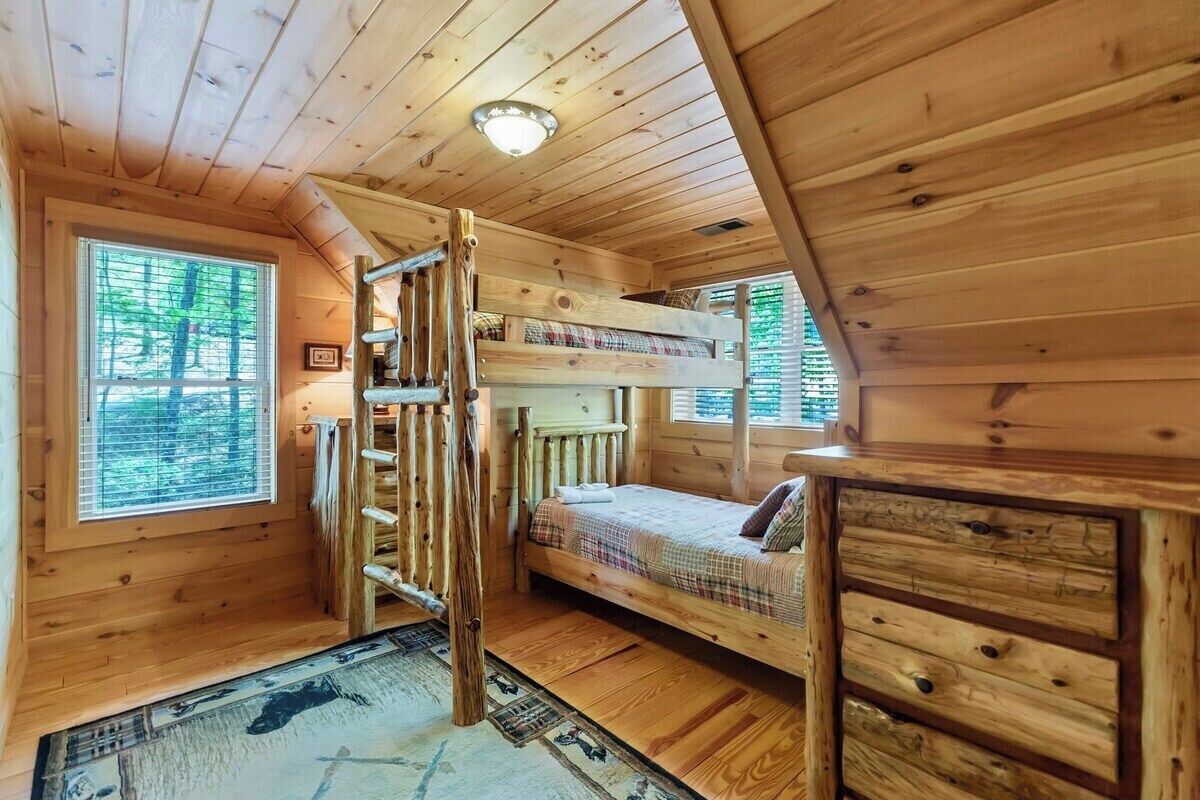 A cabin with a bunk bed, a wooden desk, and a window with blinds.