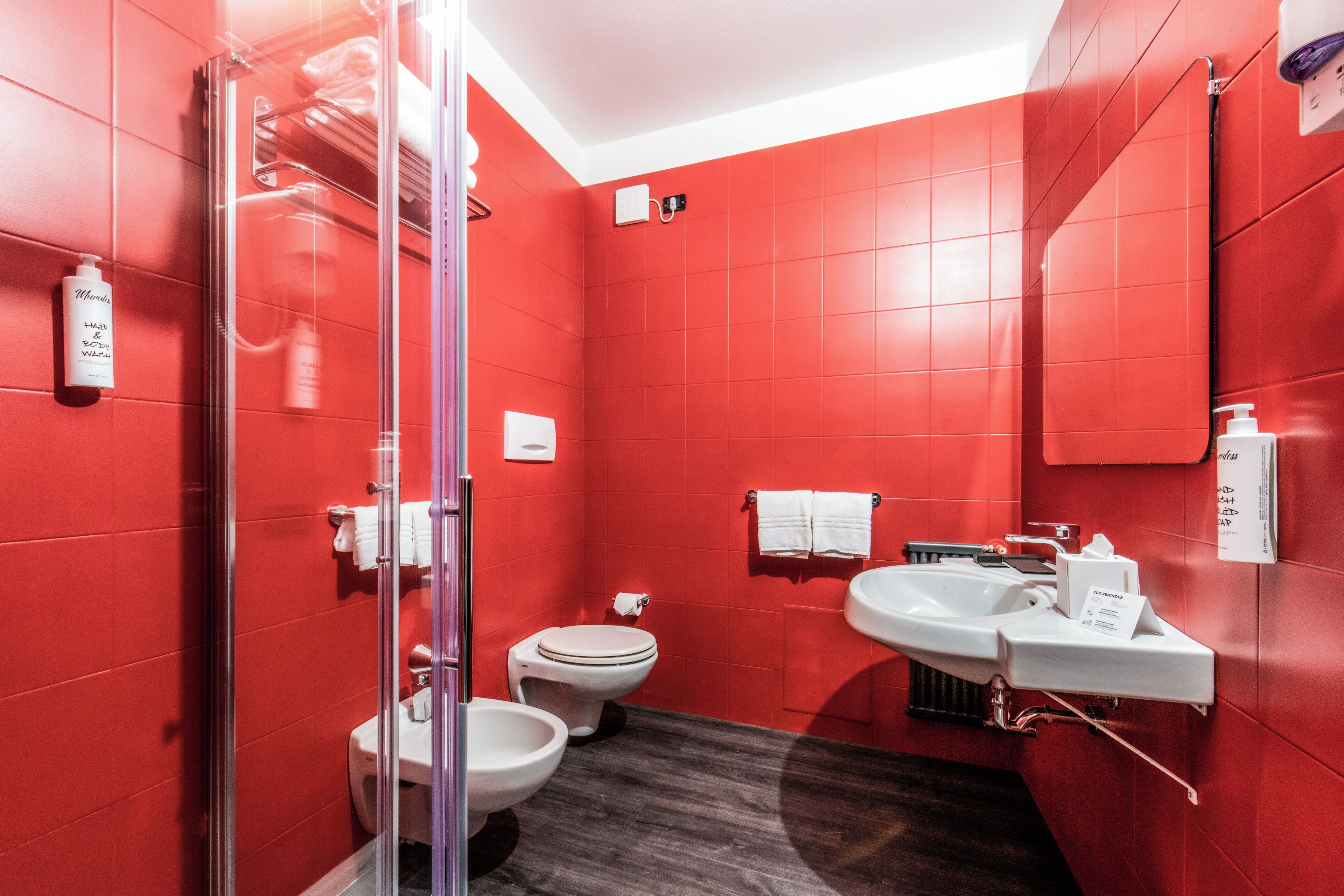 A modern bathroom with red walls, a glass shower enclosure, a toilet, and a sink with a mirror.