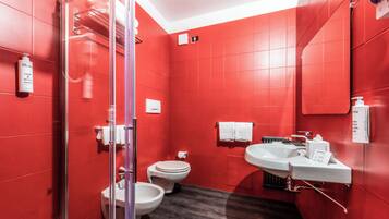 A modern bathroom with red walls, a glass shower enclosure, a toilet, and a sink with a mirror.