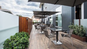 Un patio al aire libre con mesas, sillas, sombrillas y una valla de madera.