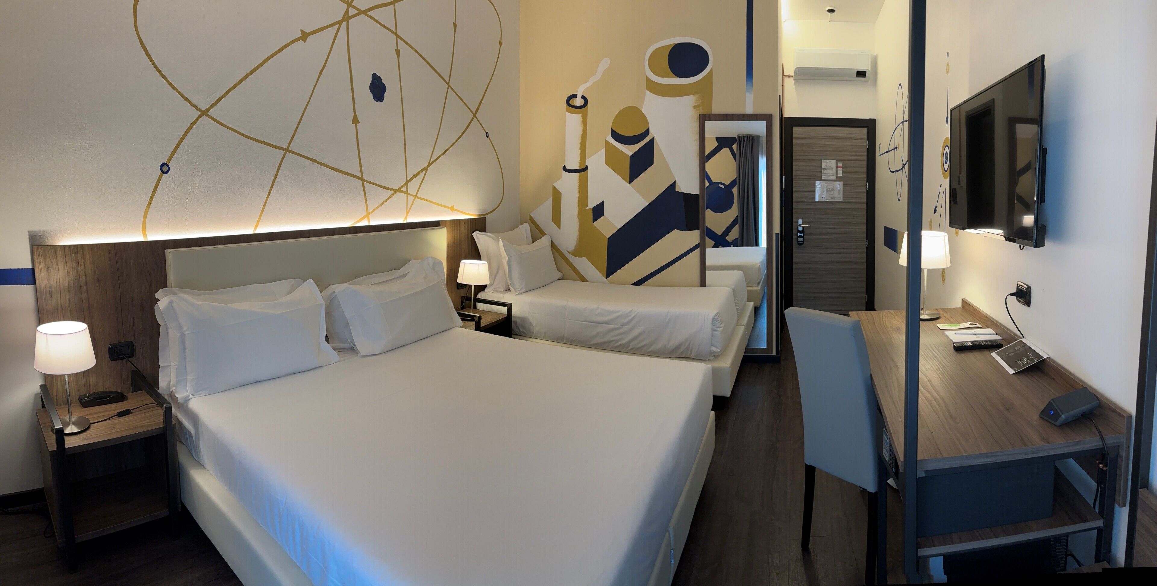 Habitación de hotel con una cama grande, un escritorio con silla, un televisor y una pared decorada con arte abstracto.