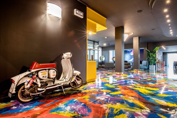 A modern interior with a colorful floor, a white scooter, and a bright yellow accent wall.