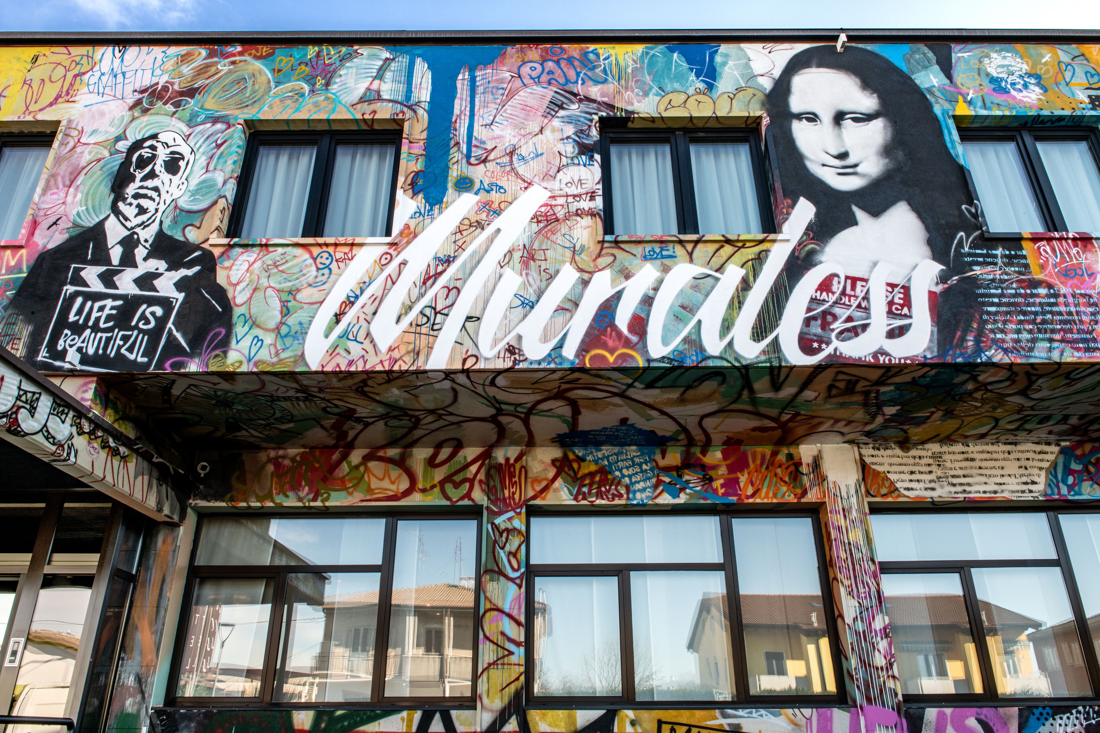 A building facade covered with colorful graffiti and murals, including a prominent depiction of the Mona Lisa.