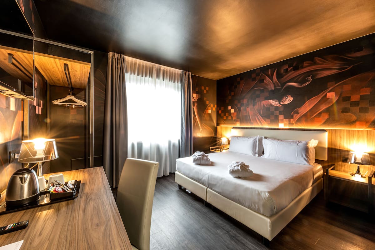 A hotel room with a large bed, bedside tables with lamps, a desk with a coffee maker, and a wardrobe.