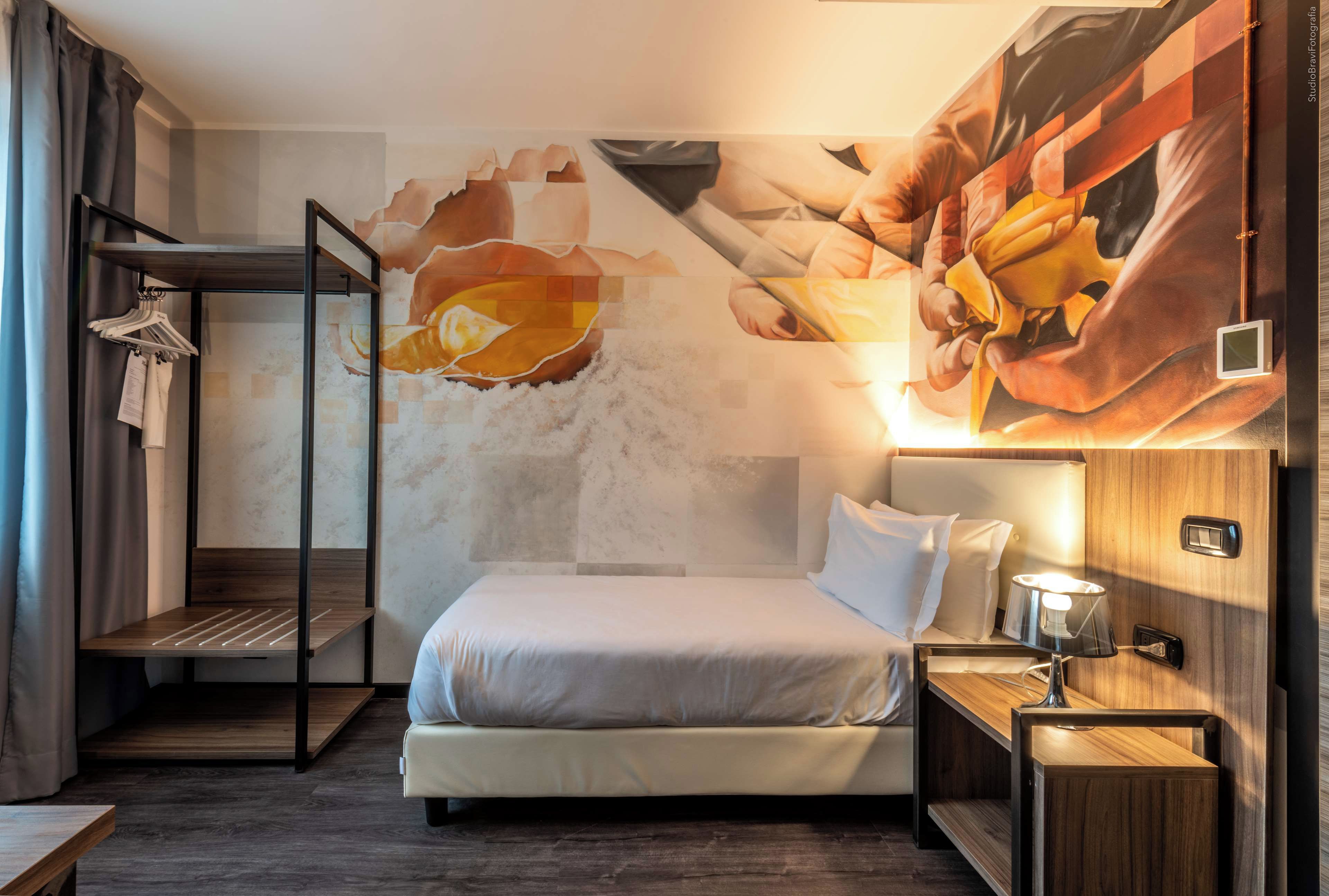 Una habitación de hotel moderna con una litera, una mesita de noche con lámpara y un gran mural abstracto en la pared.
