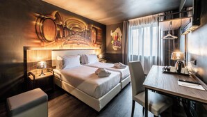 Habitación de hotel con una cama grande, dos mesitas de noche, un escritorio con una silla, un televisor y un mural en la pared con barricas de vino.