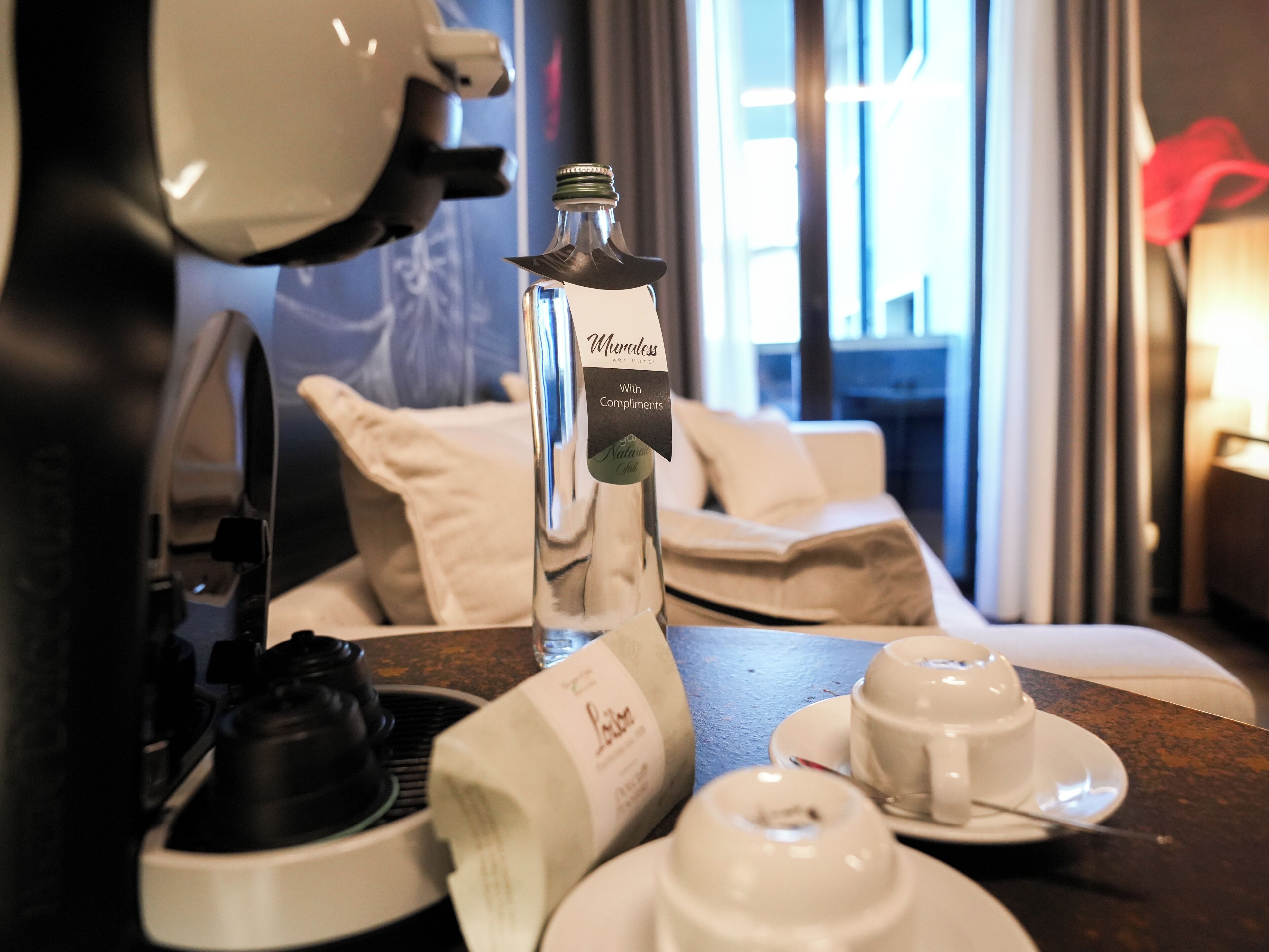 A coffee machine, a bottle of water, and tea cups on a table in a hotel room.