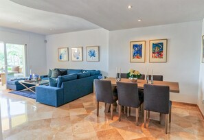 Un salon moderne avec un canapé bleu, une table à manger entourée de chaises et des œuvres d’art encadrées accrochées aux murs.
