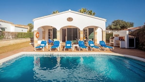 A pool area with a white building, blue lounge chairs, and a clear blue pool. - Chalet Villa El Pinar 5 with Pool, Wi-Fi, Terraces & Garden (Ciutadella de Menorca)