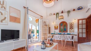 A spacious living area with a TV, dining table, chairs, and a bed. - Chalet Villa El Pinar 5 with Pool, Wi-Fi, Terraces & Garden (Ciutadella de Menorca)