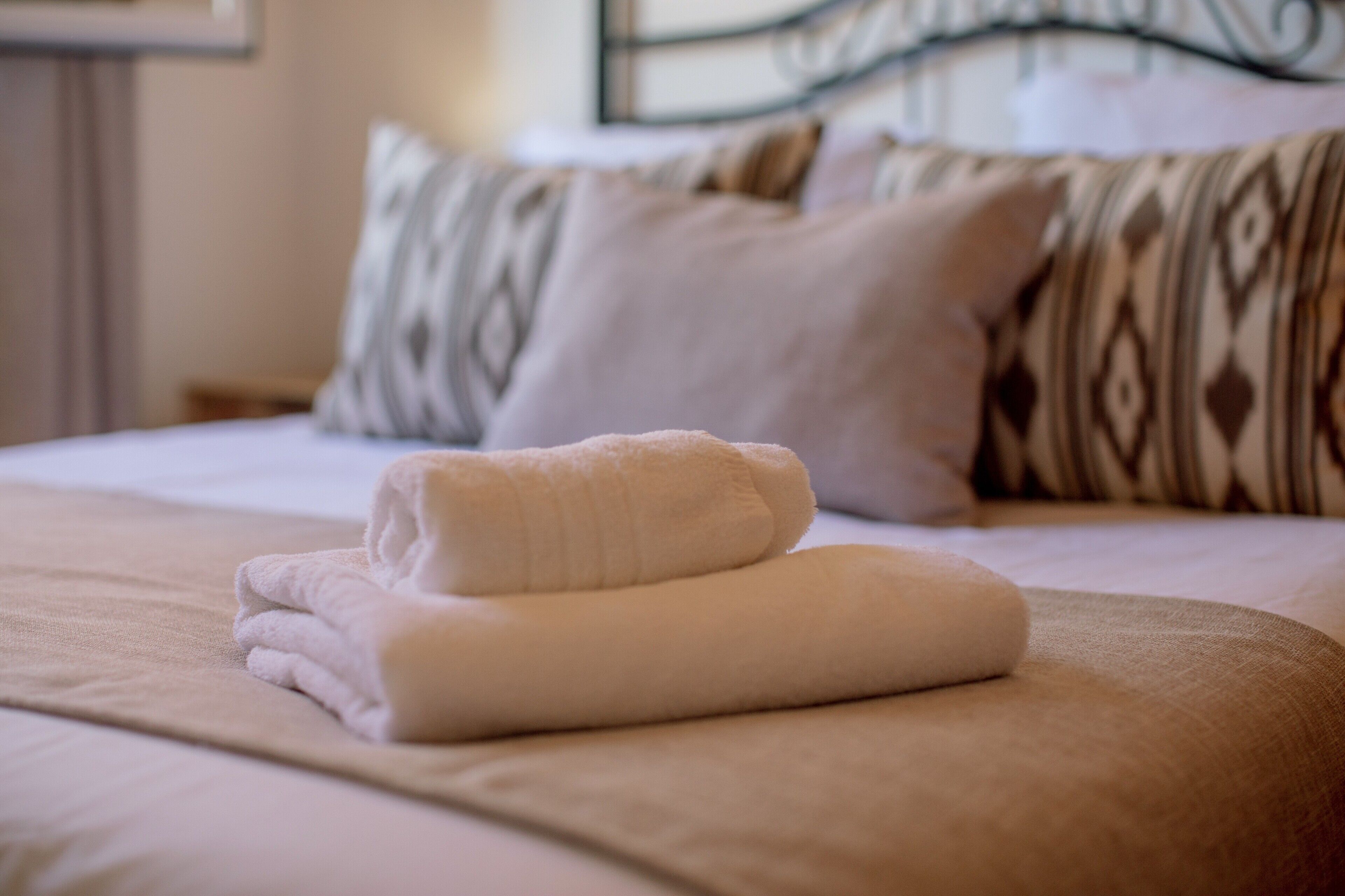 Een opgemaakt bed met een gevouwen handdoek en een kussen met dessin.
