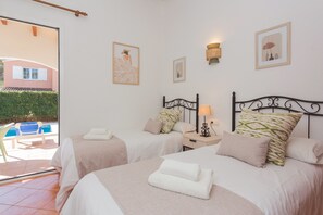 Ein Hotelzimmer mit zwei Betten, einem kleinen Nachttisch mit Lampe und Blick auf einen Swimmingpool.