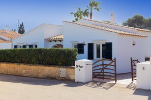 A white building with a tiled roof, a gate, and a hedge.