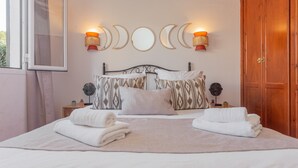 A neatly made bed with pillows, a bedside table with a lamp, and a wall with decorative moon-shaped mirrors. - 'Villa El Pinar 3' with Pool, Wi-Fi, Garden & Terrace (Ciutadella de Menorca)