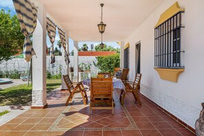 A covered patio with a table and chairs, a hanging light fixture, and a window with bars. - Pet-Friendly 'Casa Caramá' with Pool, Garden & Wi-Fi (Barbate)