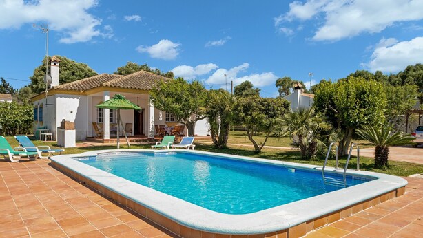 A swimming pool with a tiled deck, a small building with a tiled roof, and green trees in the background. - Pet-Friendly 'Casa Caramá' with Pool, Garden & Wi-Fi (Barbate)