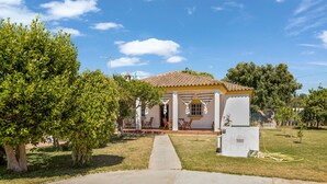 A house with a tiled roof, a porch with chairs, and a lawn. - Pet-Friendly 'Casa Caramá' with Pool, Garden & Wi-Fi (Barbate)