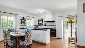 A kitchen with a dining area, white tiles, a large window, and a view of greenery outside. - Pet-Friendly 'Casa Caramá' with Pool, Garden & Wi-Fi (Barbate)