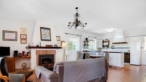 A living room with a fireplace, a sofa, a television, and a kitchen area with a white countertop and cabinets. - Pet-Friendly 'Casa Caramá' with Pool, Garden & Wi-Fi (Barbate)