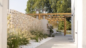 Een pad dat leidt naar een gebouw met een stenen muur, een pergola met verlichting en een witte hekken.