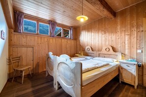 A wooden room with a bed, a chair, a nightstand, and a window with curtains.