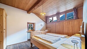 Una habitación con paneles de madera, una cama, una ventana con cortinas, un radiador y techo de madera.
