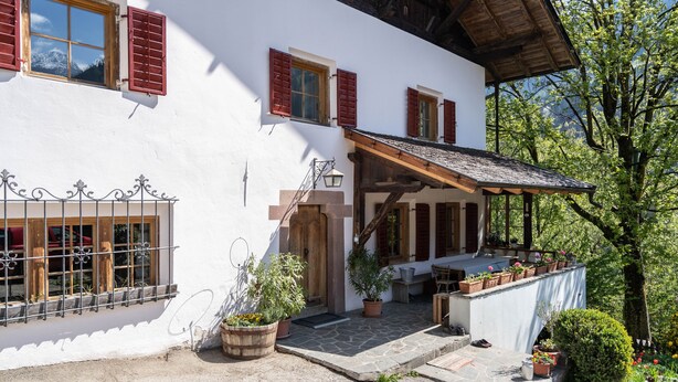 Una chaleta tradicional con terraza de piedra, contraventanas de madera y plantas en macetas.